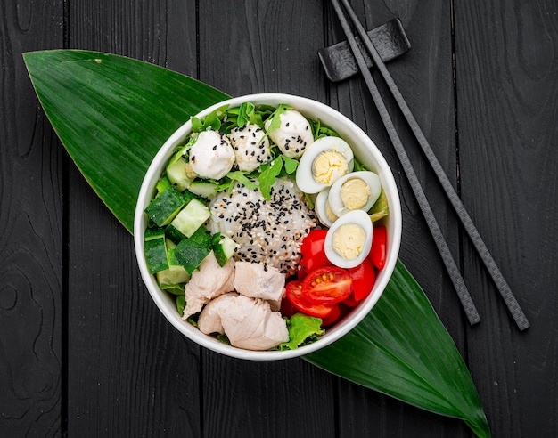 Poke bowl with chicken rice avocado cucumber cream cheese tomato and quail egg on dark background