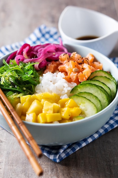 Poke bowl con riso salmonecetriolomangoonionwakame insalata semi di papavero e semi di girasoli su sfondo di legno