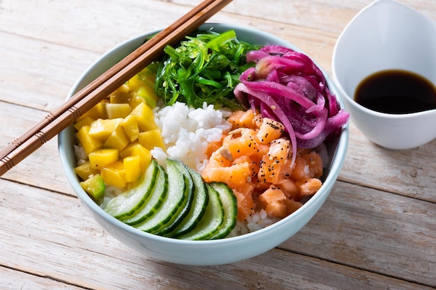 Poke bowl con riso salmonecetriolomangoonionwakame insalata semi di papavero e semi di girasoli su sfondo di legno