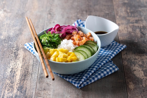 Poke bowl with rice salmoncucumbermangoonionwakame salad poppy seeds ands sunflowers seeds on wooden background