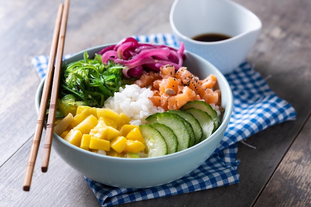 Poke bowl with rice salmoncucumbermangoonionwakame salad poppy seeds ands sunflowers seeds on wooden background