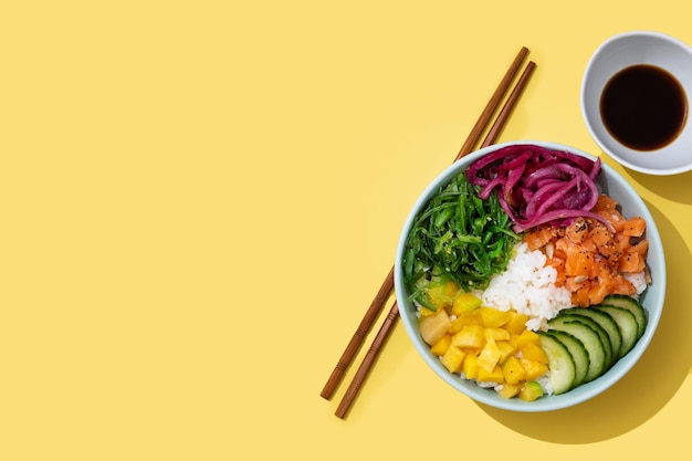 Poke bowl with rice salmoncucumbermangoonionwakame salad poppy seeds ands sunflowers seeds on yellow background