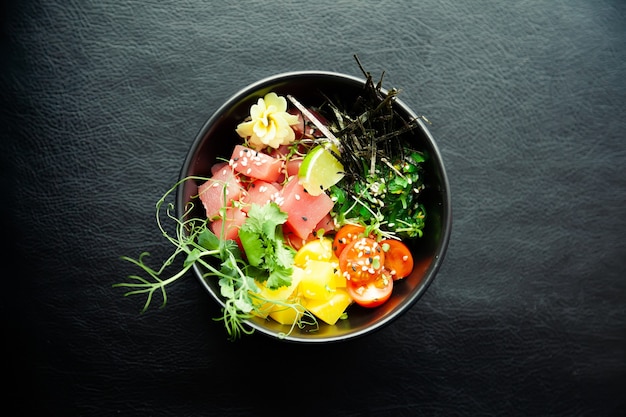 Poke salad with tuna in a bowl. ingredients fresh tuna, cherry\
tomatoes, marinated seaweed, rice, takuan, ponzu sauce, teriyaki\
sauce, nori, sesame seeds, lime, cilantro. asian seafood salad\
concept.
