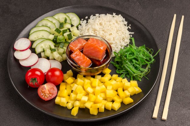 Poke Salade met rijst, radijs en zeewier in zwarte plaat. Aziatisch eten. Bamboe eetstokjes