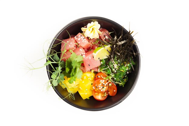Poke salade met tonijn in een kom. Ingrediënten verse tonijn, cherrytomaatjes, gemarineerd zeewier, rijst, takuan, ponzu-saus, teriyakisaus, nori, sesamzaadjes, limoen, koriander. Aziatische zeevruchten salade concept.