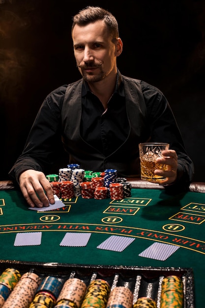 Poker player. Young guy in the casino at the gaming table. Man gambling, card games. Cards, chips, whiskey, cigarettes, poker, card game, gambling - gambling concept.