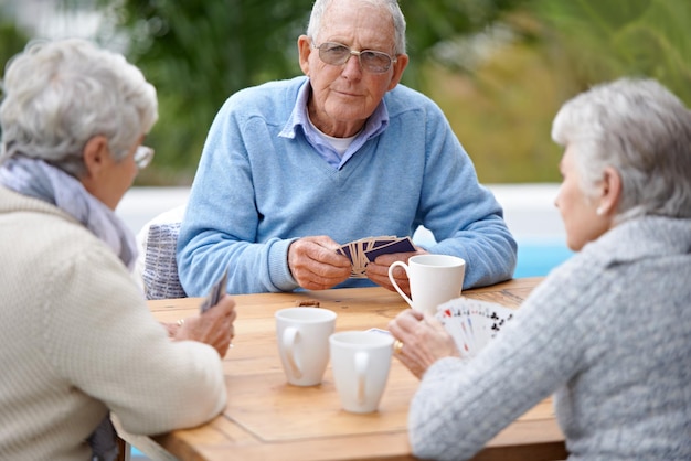 Poker playing cards and senior group in retirement outdoor and relaxed in garden backyard and terrace Elderly people bridge and smile with coffee table and outside for relaxation fun and games