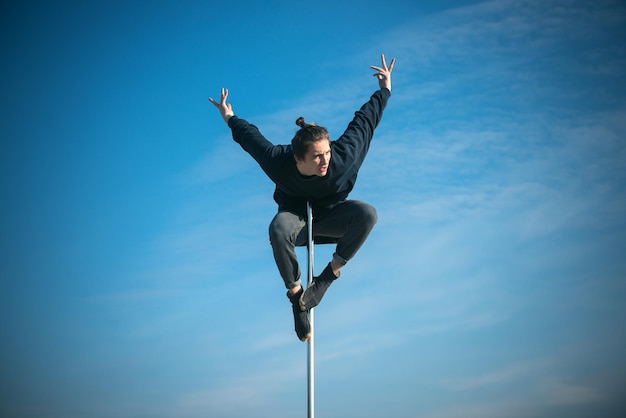 Pole dance uomo in forma che si esercita con il pilone all'aperto