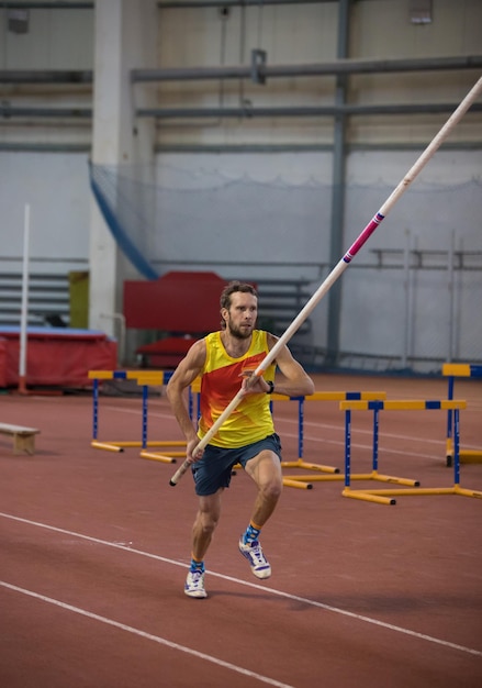 Pole vaulting indoors a man in yellow shirt running on the track with a pole in the stadium