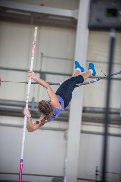 Pole vaulting indoors young woman with pigtails jumping over the partition leaning on the pole