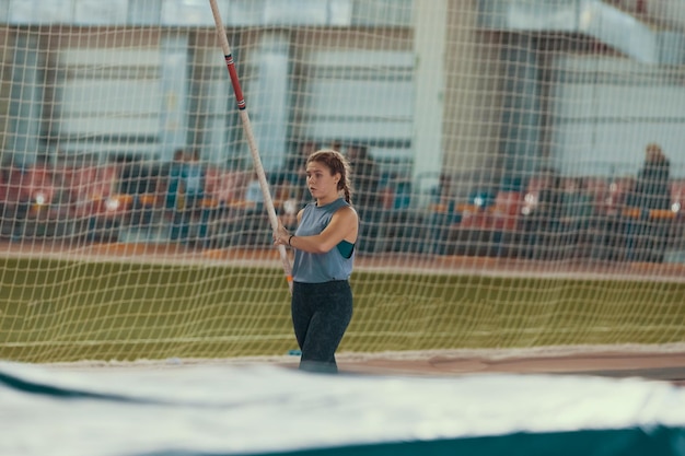 Pole vaulting indoors young woman with pigtails standing near the mat holding a pole