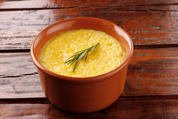 Polenta in ceramic bowl on rustic wooden table Cream of corn or mamaliga