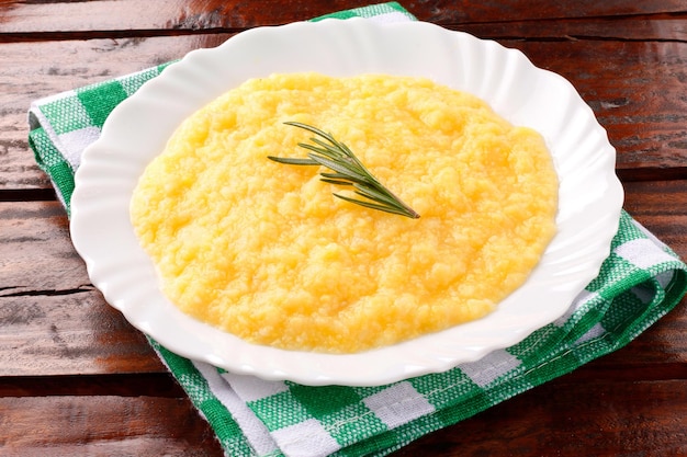 Polenta in white dish on rustic wooden table Cream of corn or mamaliga