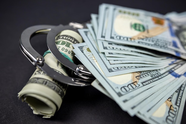 Police handcuffs lie on many dollar bills isolated on black background