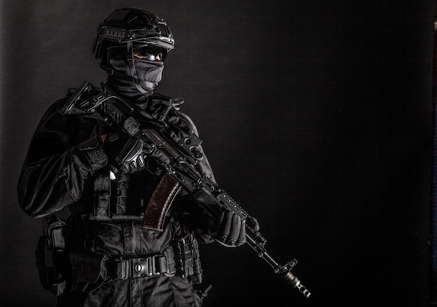 Police special forces, quick reaction team officer, tactical
group fighter in black uniforms, helmet and hidden behind mask
identity, armed with assault rifle, low key studio shoot on black
background