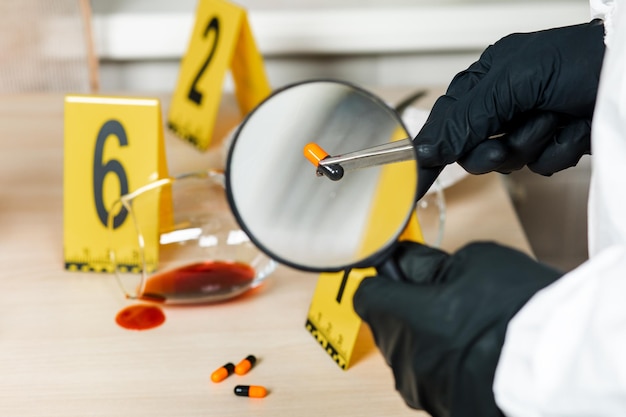 A policeman looks through a magnifying glass at the evidence at the crime scene The crime scene of poisoning and overdosing