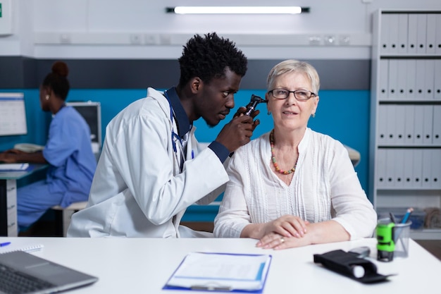 Poliklinische otoloog die senior patiënt raadpleegt die otoscoop gebruikt om oorziekte te controleren. Kliniek otologie specialist onderzoekt gepensioneerde vrouw oorpijn met behulp van otoscoop terwijl in het ziekenhuis kabinet.