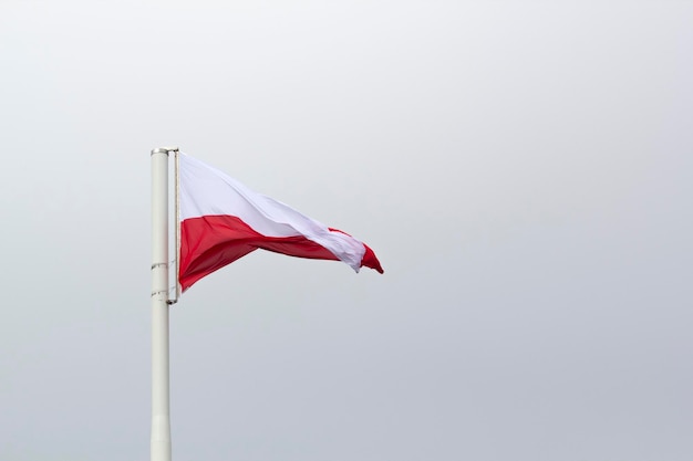 A Polish flag flies on a pole with the sky in the background