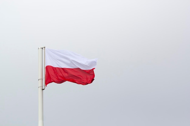 A Polish flag flies on a pole with the sky in the background