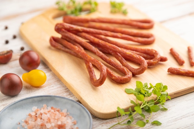 Polish smoked pork sausage kabanos on cutting board with salt and pepper on white wooden background Side view close up selective focus
