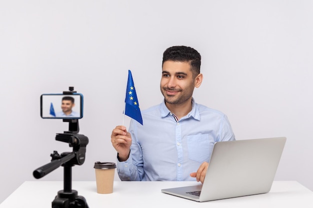 Politicus ambassadeur of advocaat die de vlag van de Europese Unie vasthoudt en lacht naar camera streaming nieuws maken politieke aankondiging over mensenrechten indoor studio shot geïsoleerd op witte achtergrond