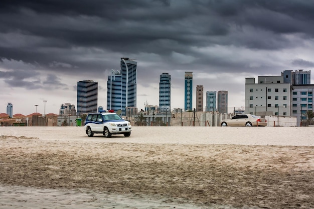 Politie off-road auto en stadssedan op een zandstrand op de achtergrond van wolkenkrabbers bij bewolkt weer