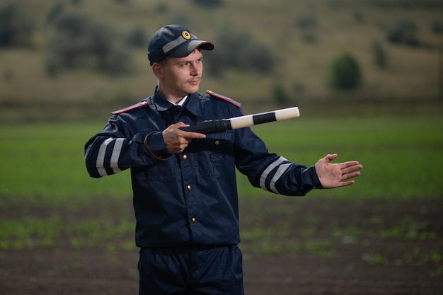 Politieagent in eenvormig met een staaf in zijn hand op de achtergrond van landelijk landschap