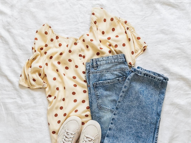 Polka dot muslin blouse blue jeans sneakers beautiful comfortable urban style womens clothing on a light background top view