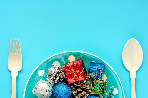 Polka dot plate of Xmas ornaments with spoon and fork on blue background for Christmas day