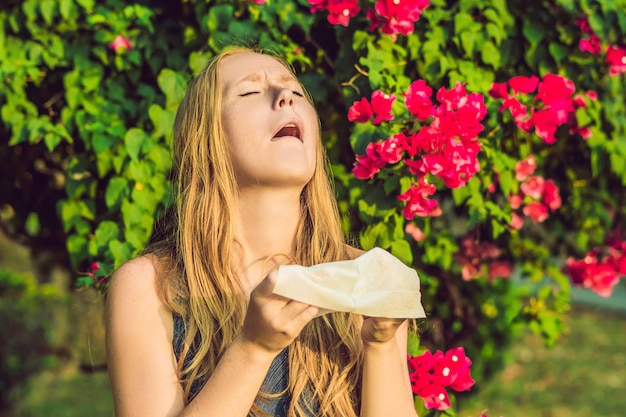 Pollen allergy concept. Young woman is going to sneeze. Flowering trees in background