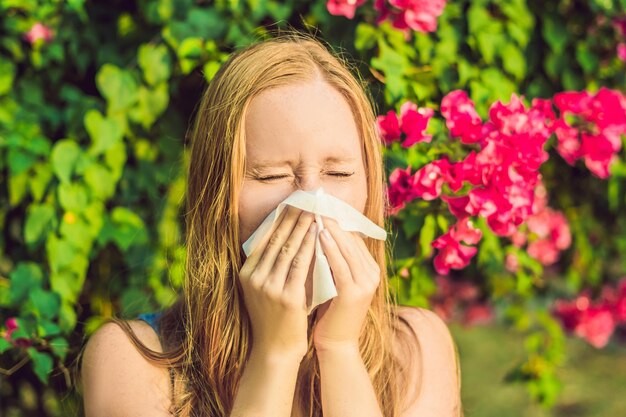 Pollenallergie concept. Jonge vrouw gaat niezen. Bloeiende bomen op de achtergrond