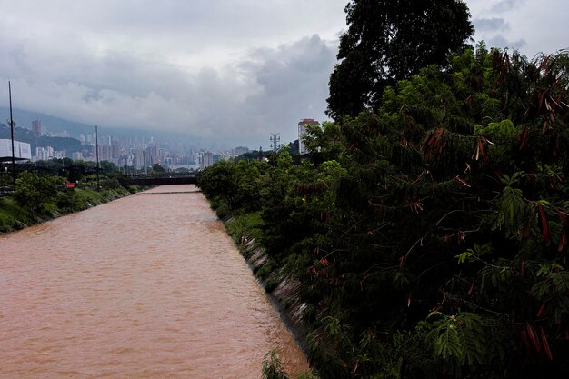 Foto fiume inquinato di medellin con un colore giallastro e piante che lo circondano e edifici sullo sfondo il cielo inquinato può essere visto verso sud della città