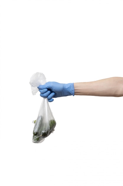 Polythene bag of cucumbers held in hand wearing blue gloves on white wall