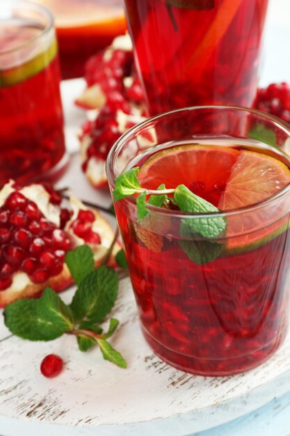 Pomegranate drink in glasses with mint and slices of orange on color wooden background