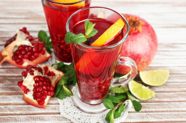 Pomegranate drink in glasses with mint and slices of orange on color wooden planks background