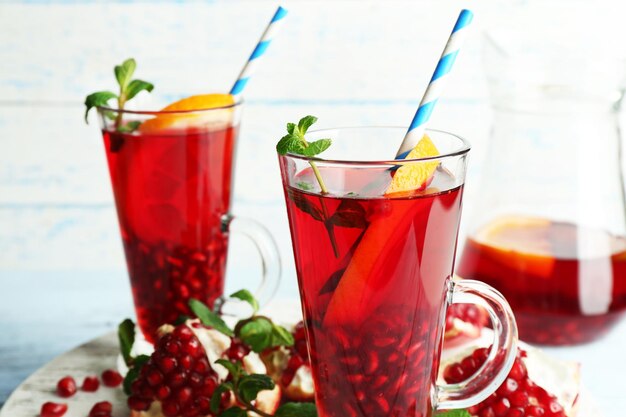 Pomegranate drink in glasses with mint and slices of orange on color wooden planks background