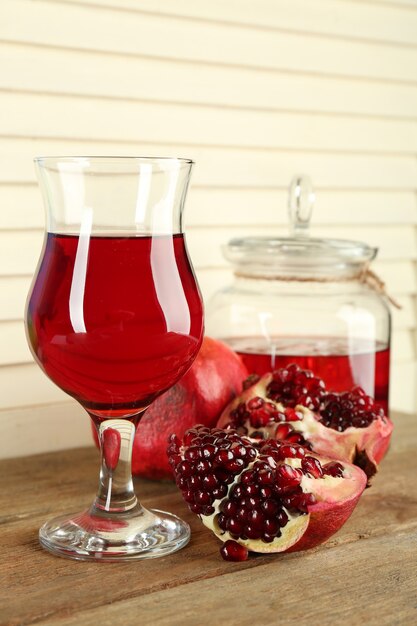 Pomegranate and glass of juice on wooden table and wight fence