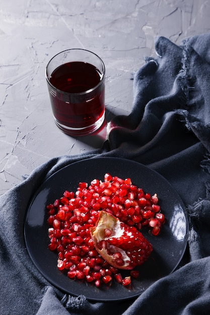 Pomegranate grains on a plate on a dark gray background with drapery and glass of juice