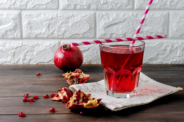 Pomegranate juice in glass and pomegranates on dark old wood