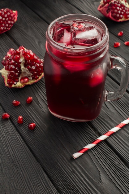 Pomegranate juice with ice in the glass on the black wooden table.