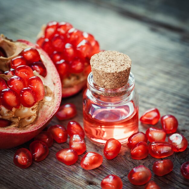 Pomegranate oil in bottle and open garnet fruit with seeds on wooden table Selective focus