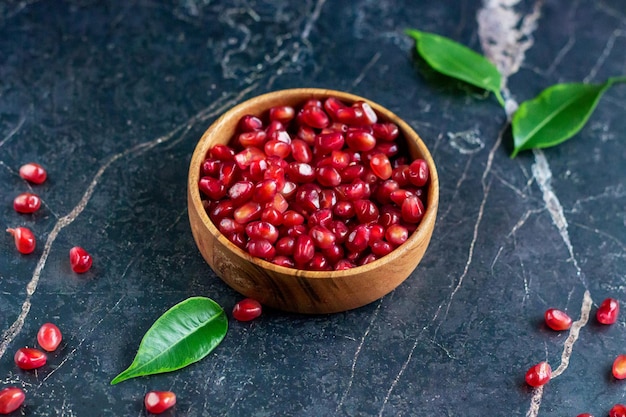 Pomegranate seeds in wood bowl with seeds on black marble table