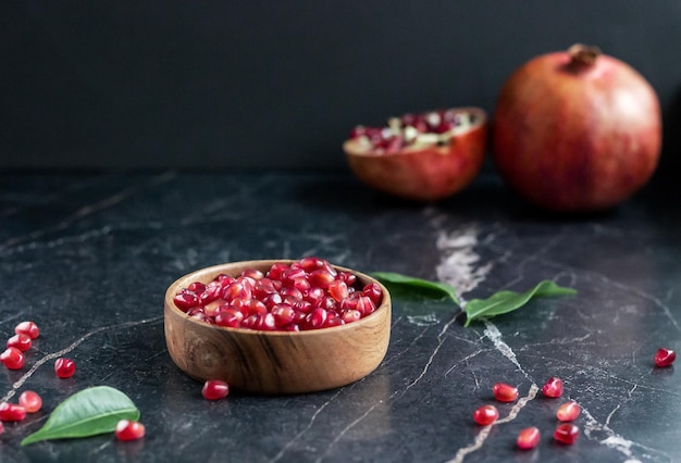 Pomegranate seeds in wood bowl with seeds on marble table with pomegranate fruit on the background