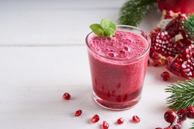 Pomegranate smoothie in a glass with fir branches and Christmas decoration
