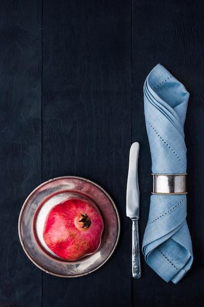 Pomegranate on the vintage metal plate with knife and napkin vertical