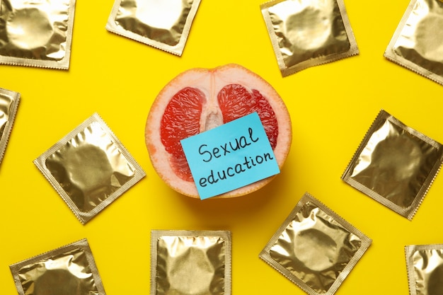 Photo pomelo with text sexual education and condoms on yellow surface