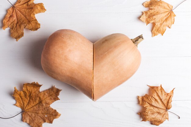 Pompoen gesneden in de vorm van een hart en gele bladeren, herfst en gewas.