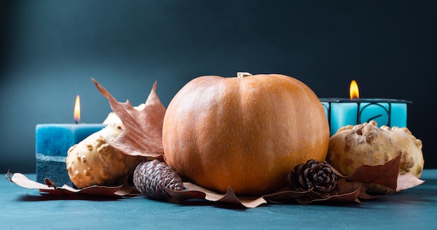 Pompoen op blauw met kaarsen en herfstbladeren en dennenappels