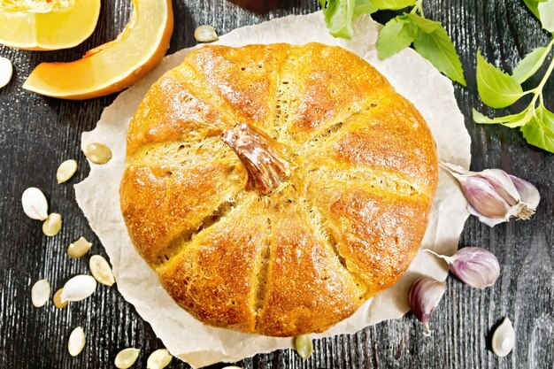 Pompoenbrood op papier, knoflook, basilicum, plakjes en zaden van een groente op een houten plankachtergrond van bovenaf