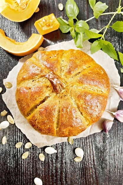 Pompoenbrood op perkament, knoflook, basilicum, plakjes en zaden van een groente op de achtergrond van een donkere houten plank van bovenaf